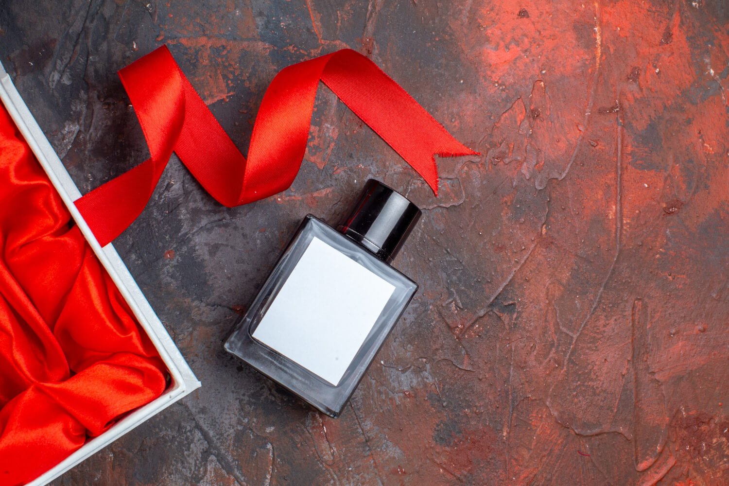 a unisex perfume on the floorwith a red ribbon and box